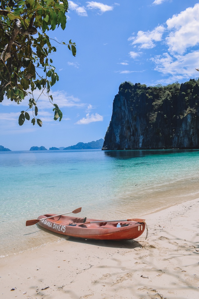 Our kayak on an empty beach in El Nido, with clear turquoise water and cliffs behind it